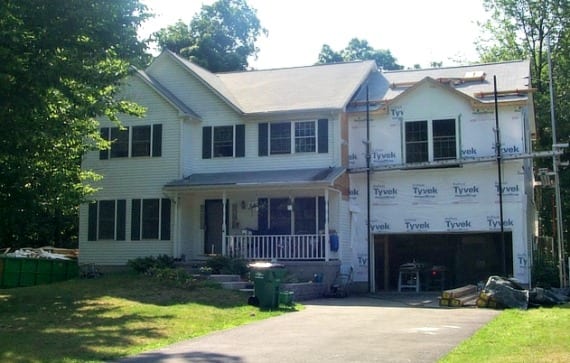 Large two-story white home with black shutters, surrounded by trees, with unfinished garage addition on the right.